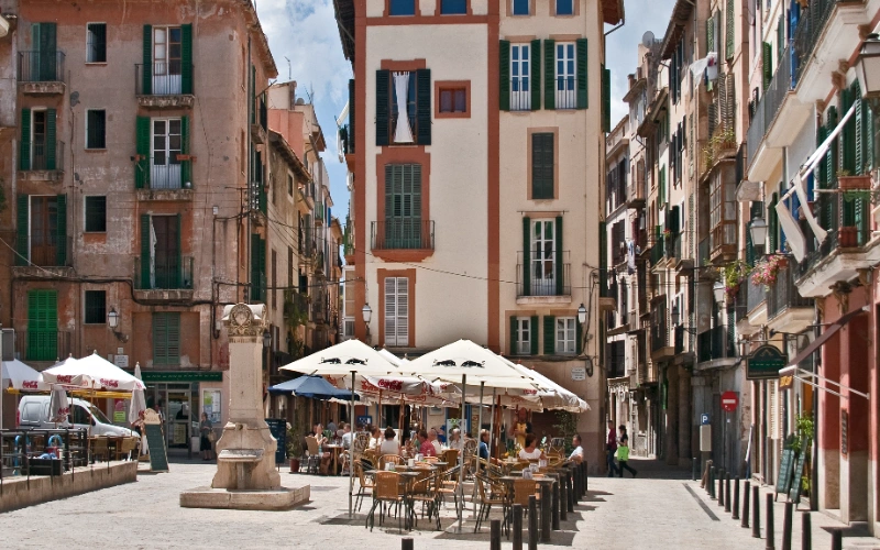 Plaza con caf&eacute;s al aire libre, rodeada de coloridos edificios antiguos.