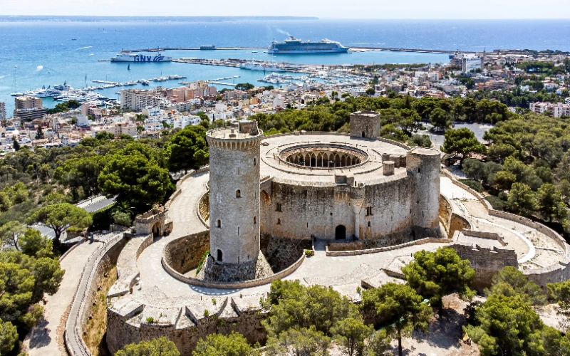 Castillo circular con vistas al puerto y la ciudad rodeado de &aacute;rboles.