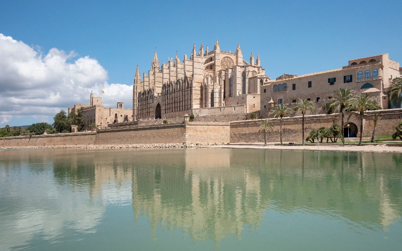 Catedral g&oacute;tica frente a un lago, cielo azul y palmeras.