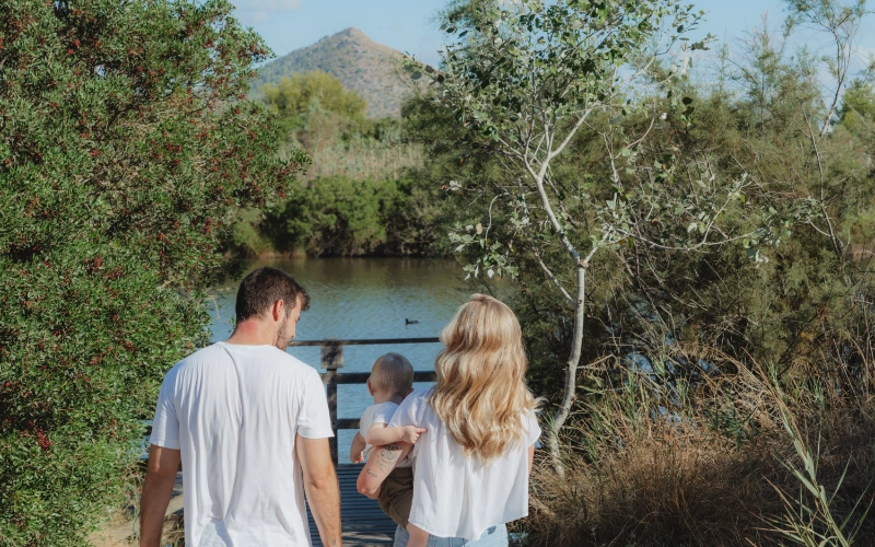 Familia paseando cerca de un lago con monta&ntilde;as al fondo.