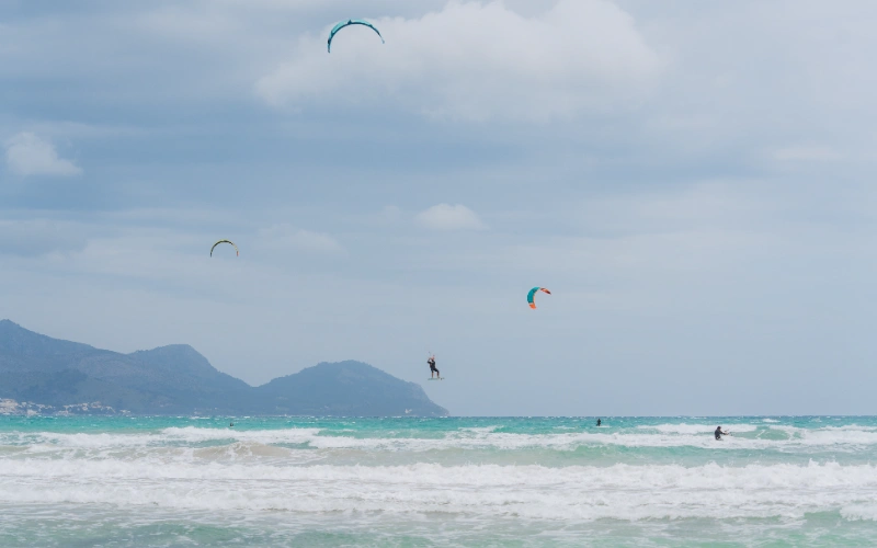 Kitesurfistas navegando en el mar con monta&ntilde;as de fondo.