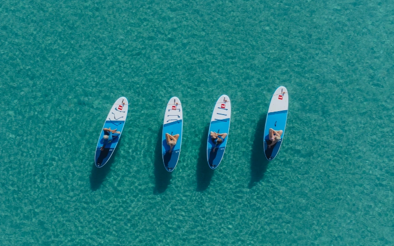 Cuatro personas descansan sobre tablas de paddle en agua turquesa clara.