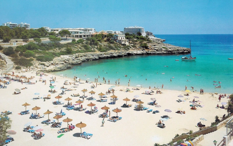 Playa con ba&ntilde;istas, sombrillas y agua turquesa bajo un cielo despejado.
