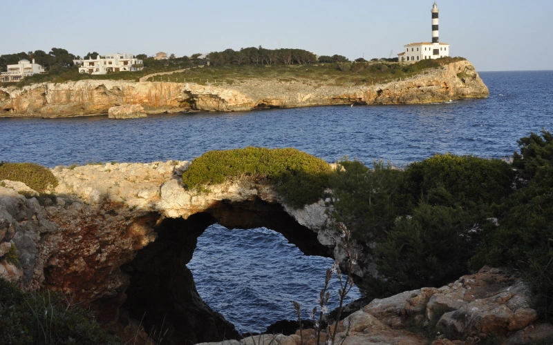 Arco de roca con mar y faro al fondo en un paisaje costero.