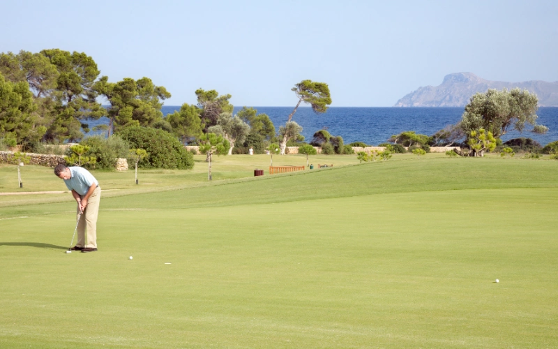 Persona jugando al golf en un campo con vista al mar y &aacute;rboles alrededor.