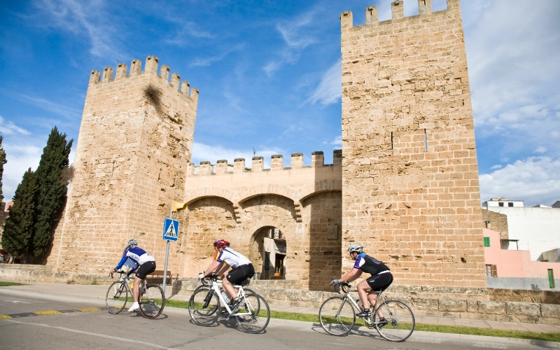Ciclistas pasando frente a una hist&oacute;rica puerta de muro de piedra.
