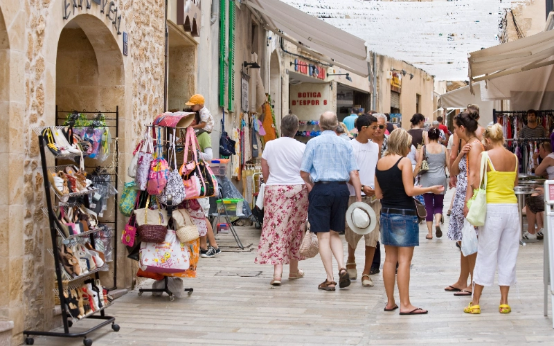Personas caminando en un mercado al aire libre con tiendas y bolsas colgando.