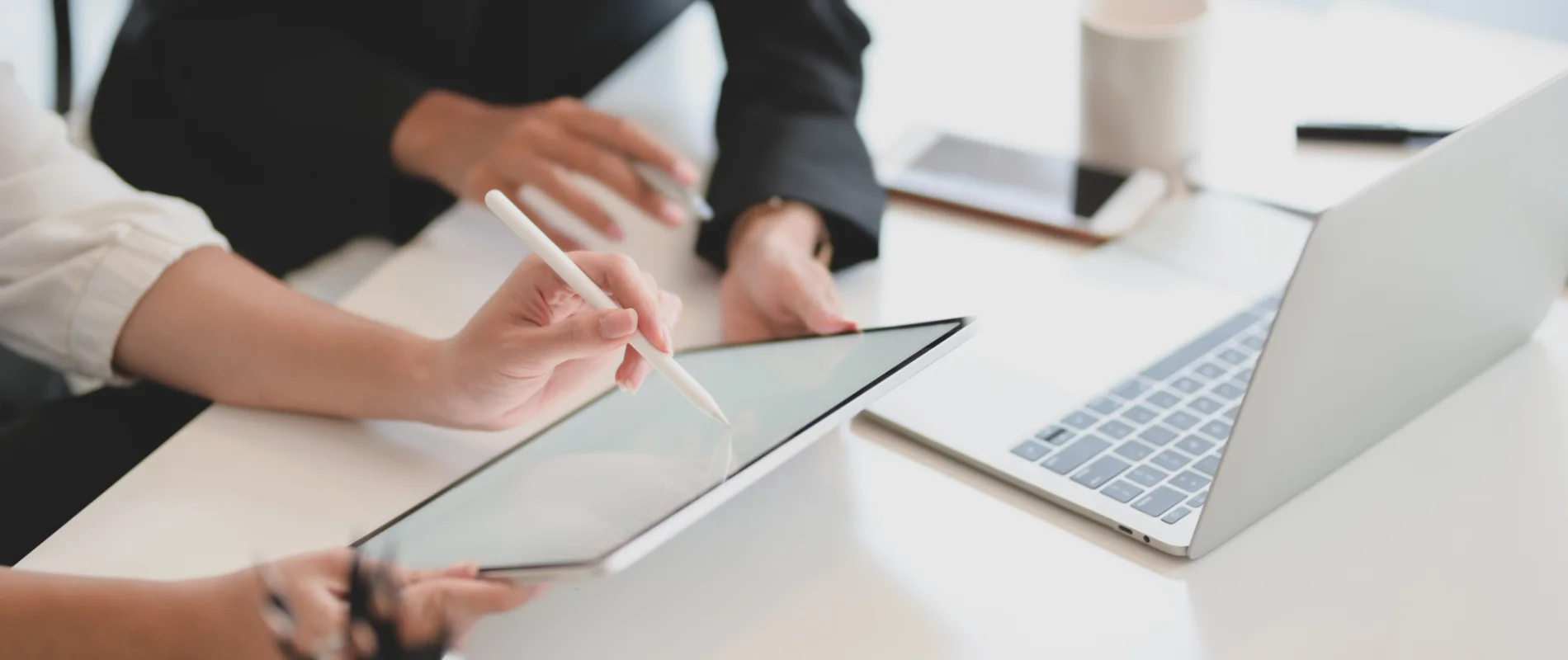 Manos usando una tablet con l&aacute;piz, junto a una laptop abierta en un escritorio.