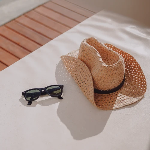 Sombrero de paja y gafas de sol sobre una superficie blanca y madera.