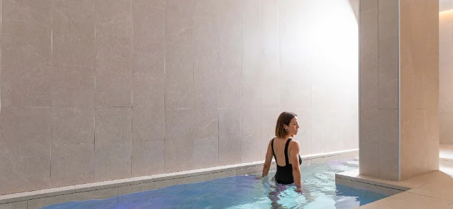 Mujer en traje de ba&ntilde;o en una piscina interior de dise&ntilde;o minimalista.