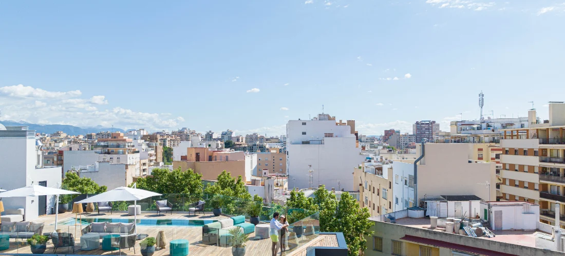 Vista de una ciudad desde una terraza con sillas y sombrillas. Cielo despejado.