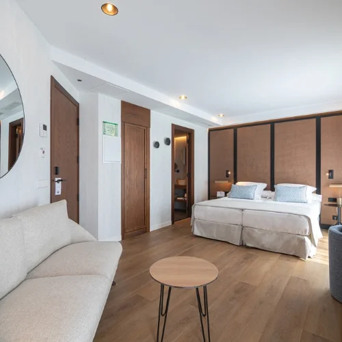 Habitaci&oacute;n moderna con cama, sof&aacute; y mesa peque&ntilde;a en tonos neutros.
