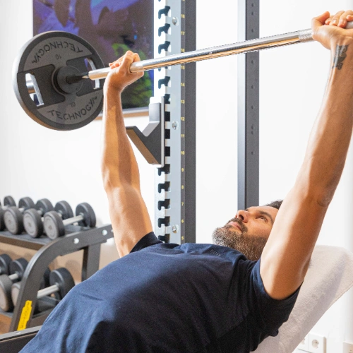 Hombre levantando pesas en banco de gimnasio.