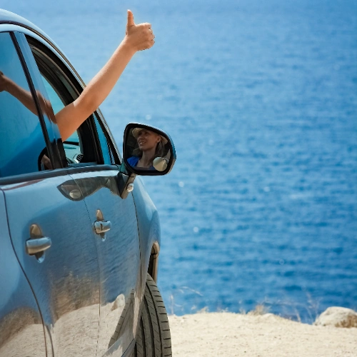 Persona en auto junto al mar levantando el pulgar en se&ntilde;al de aprobaci&oacute;n.