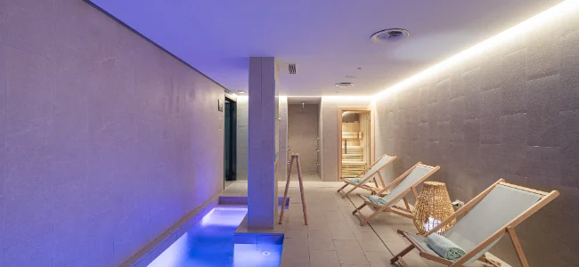 Spa moderno con sillas reclinables y piscina iluminada en ambiente sereno.