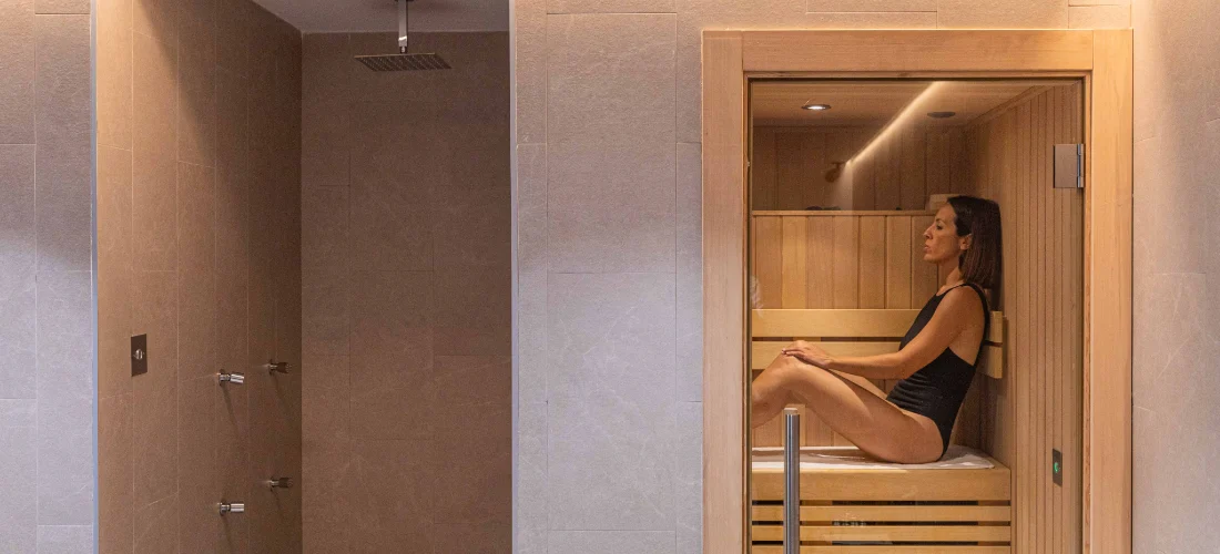 Mujer en traje de ba&ntilde;o relaj&aacute;ndose en una sauna de madera.