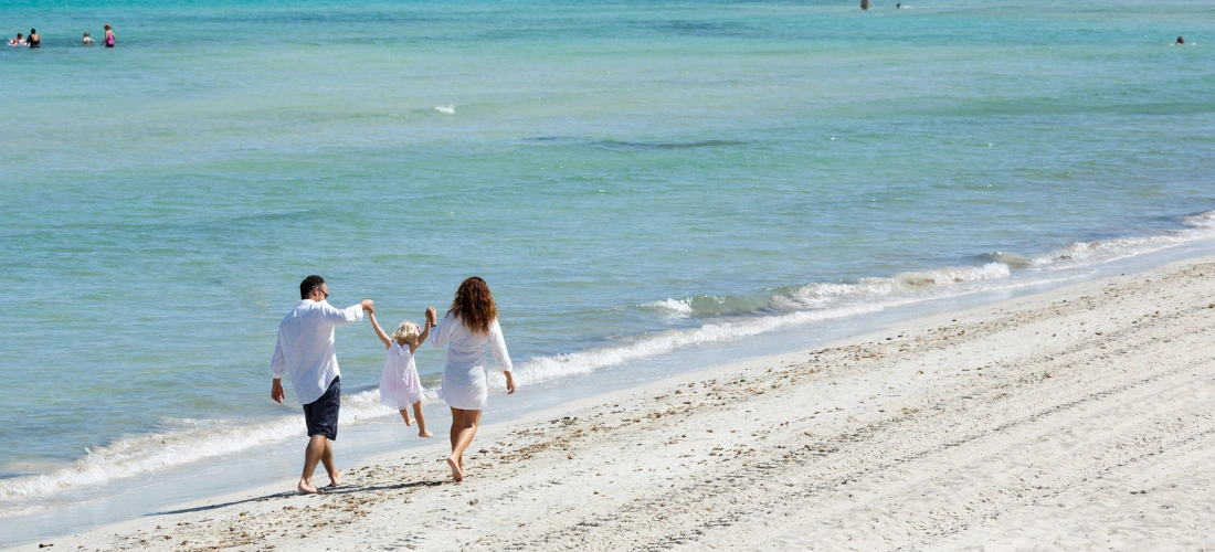 Familia caminando en la playa bajo el sol, junto al mar.