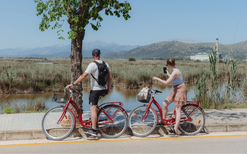 Dos personas en bicicleta junto a un lago, una de ellas tomando una foto.