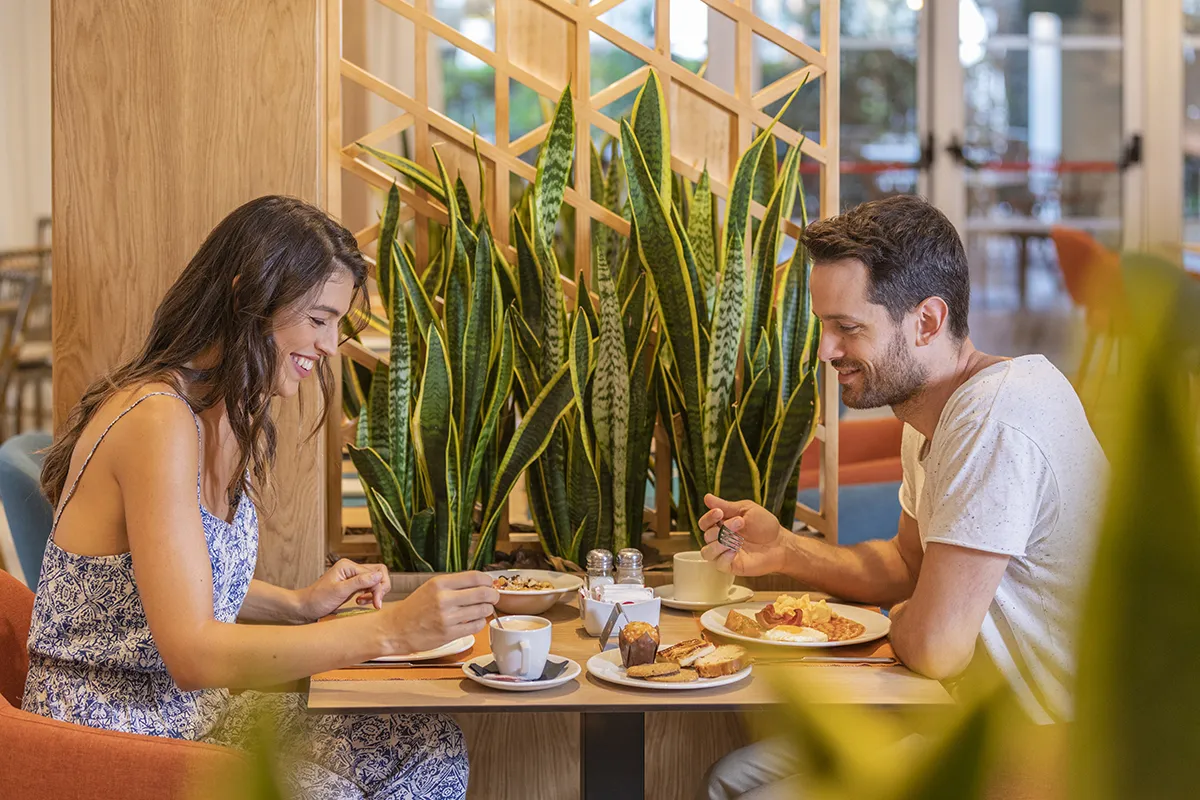 Pareja desayunando en un restaurante cerca de plantas decorativas.
