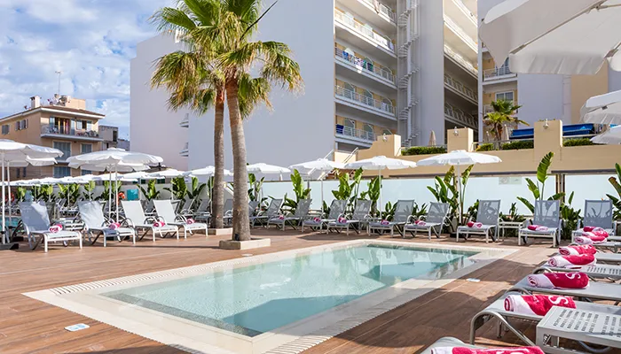 Piscina al aire libre rodeada de tumbonas y sombrillas en un hotel.