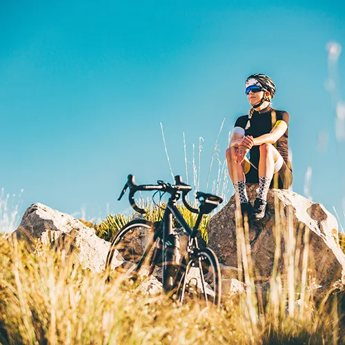 Ciclista descansando sobre una roca junto a su bicicleta en un entorno natural.