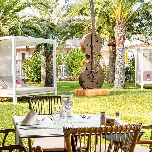 Terraza de restaurante con jard&iacute;n, esculturas y palmeras de fondo.
