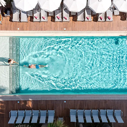 Piscina con personas nadando y tumbonas alrededor. Vista a&eacute;rea.
