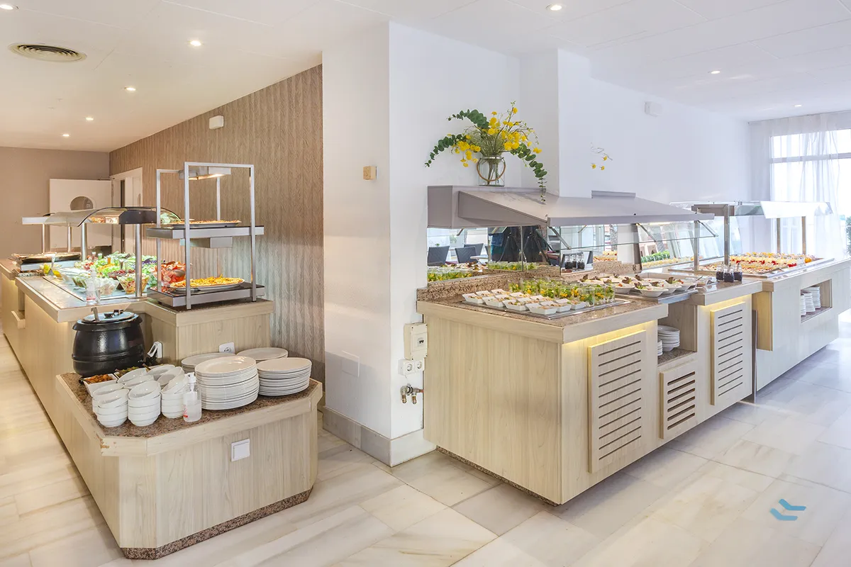 Buffet variado en comedor iluminado con techos altos.