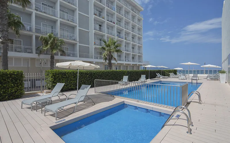 Piscina junto a edificio de apartamentos, con tumbonas y sombrillas.