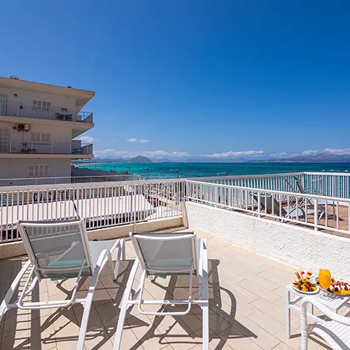 Terraza con sillas y vista al mar, edificio al fondo.