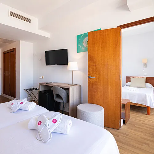 Habitaci&oacute;n de hotel con camas, televisor, escritorio y puerta a otra habitaci&oacute;n.