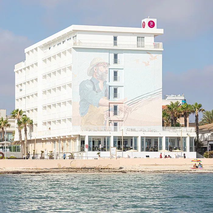Edificio de hotel blanco con mural de un hombre pescando cerca de la playa.