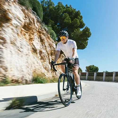 Ciclista en carretera con fondo de roca y &aacute;rboles bajo un cielo despejado.