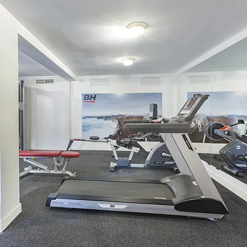 Gimnasio con caminadora, bicicleta est&aacute;tica y banco de pesas al fondo.