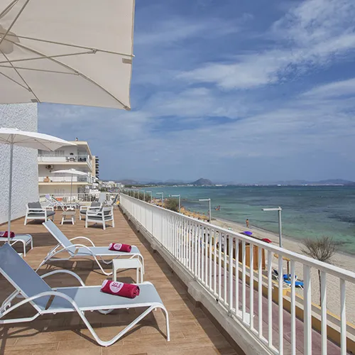 Terraza con tumbonas y sombrillas frente a la playa bajo un cielo parcialmente nublado.