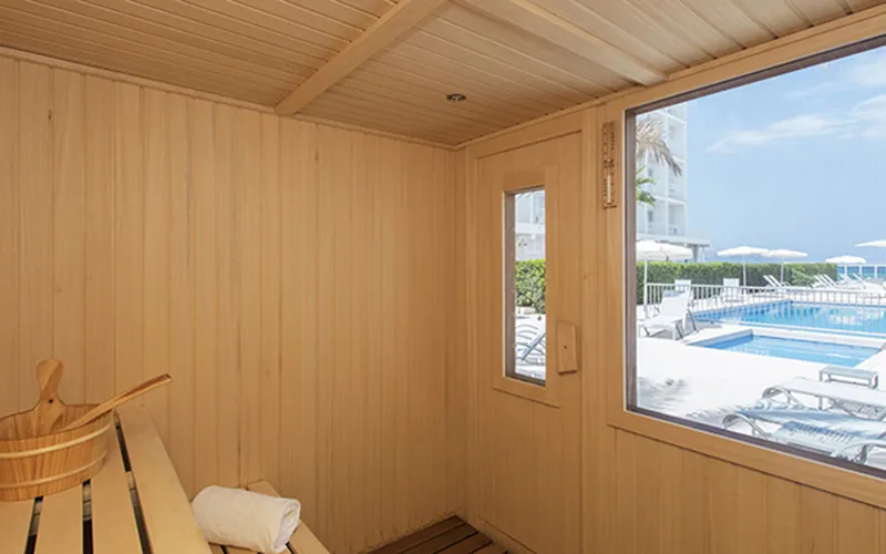 Sauna de madera con vista a una piscina exterior y cielo azul despejado.