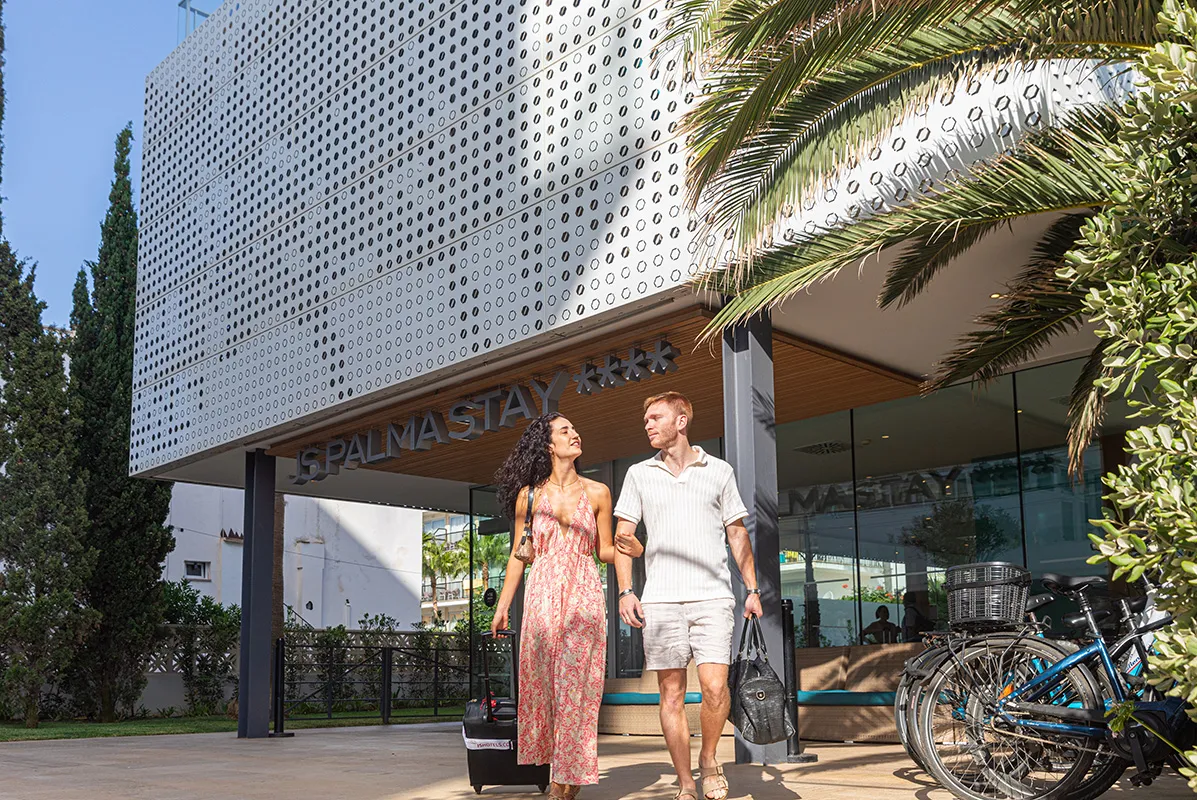 Pareja con maletas saliendo del hotel Palma Stay en un d&iacute;a soleado.