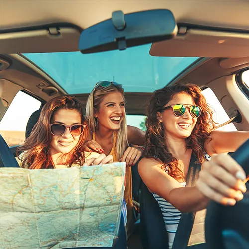 Mujeres j&oacute;venes riendo en un coche con un mapa en un viaje por carretera.
