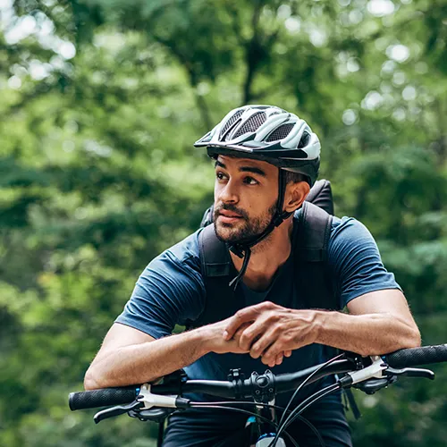Hombre con casco descansa en bicicleta en un entorno natural.