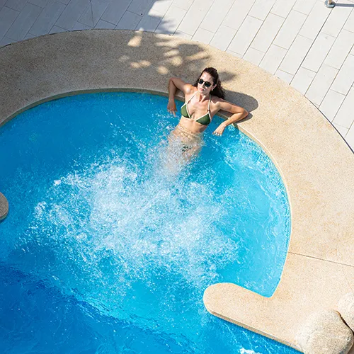 Mujer en piscina redonda con bordes de piedra, vista desde arriba.