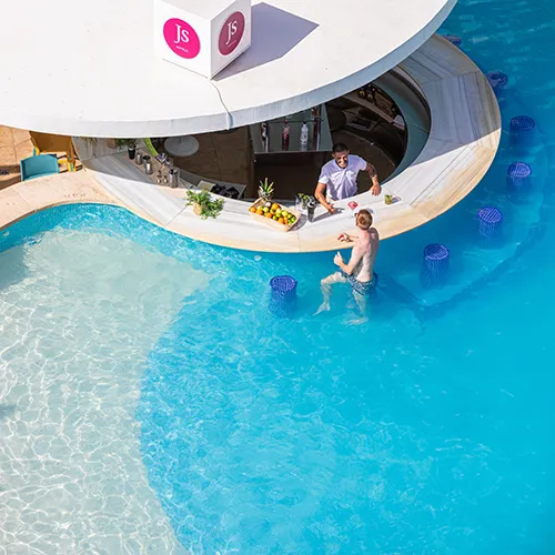 Persona en bar de piscina, rodeado de agua azul y taburetes sumergidos.