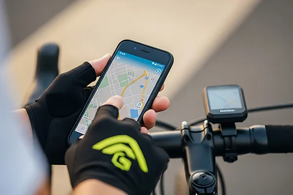 Manos en guantes negros usan GPS en celular sobre una bicicleta.