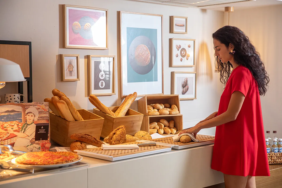 Mujer en buffet de pan y reposter&iacute;a junto a una pared de cuadros.