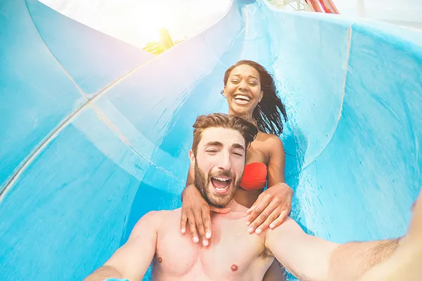 Pareja bajando por un tobog&aacute;n de agua, sonrientes y disfrutando.