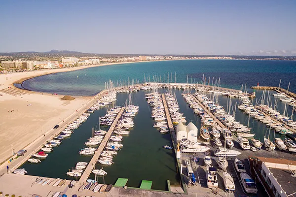 Puerto lleno de barcos y la playa con el mar al fondo bajo el cielo despejado.