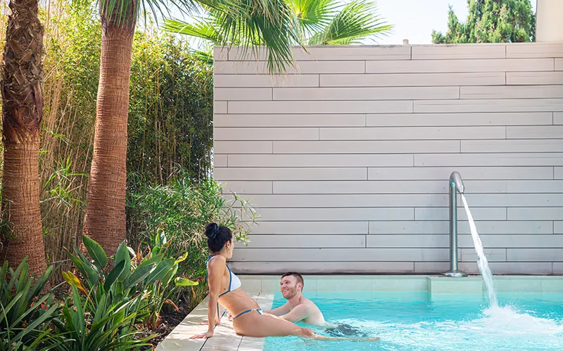 Pareja en la piscina junto a palmeras y pared de madera.