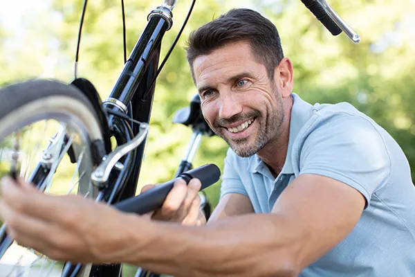 Hombre sonriente ajustando la rueda de una bicicleta en el parque.