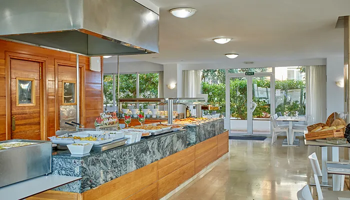 Buffet en un comedor moderno y luminoso, con mesas y sillas al fondo.