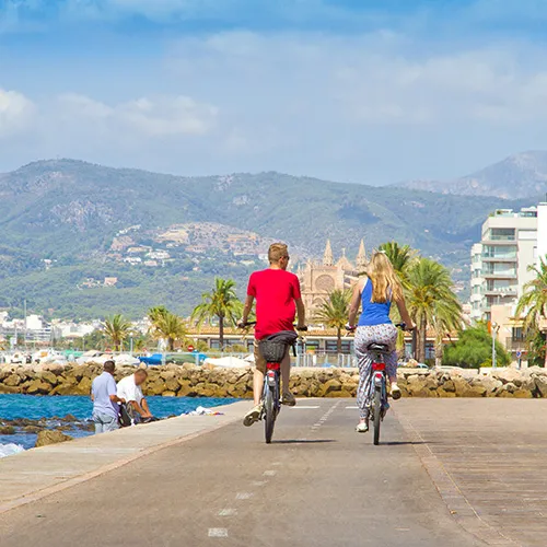 Dos personas andando en bicicleta por el paseo mar&iacute;timo frente a las monta&ntilde;as.