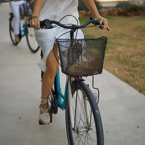 Mujer en bicicleta con cesta negra en el frente, pedalea por un camino.